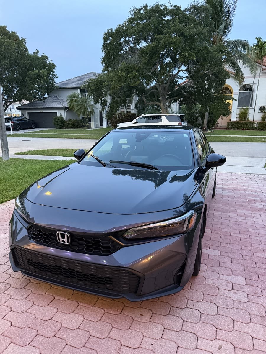 A graphite Honda Civic on a paver driveway, paint holding a clean reflection after a detail